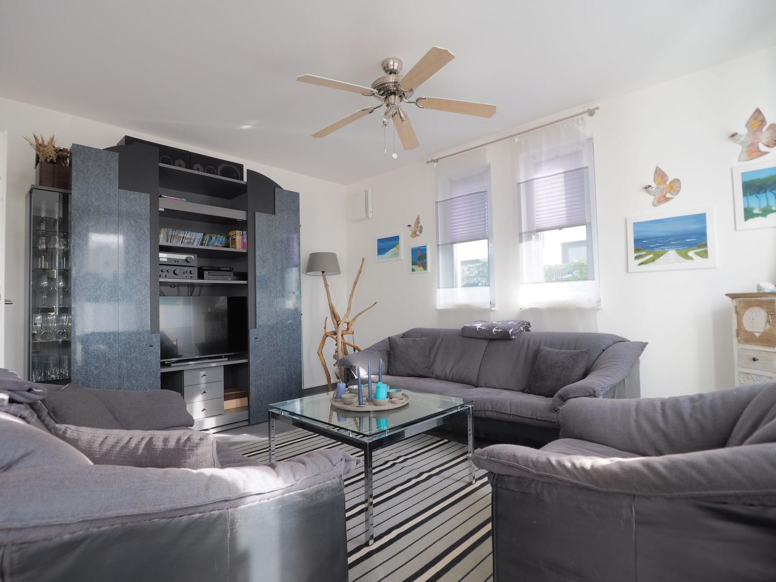 Wohnzimmer mit grauem Sofa, Glas-Tisch und Fernseher in schwarzem Schrank.
