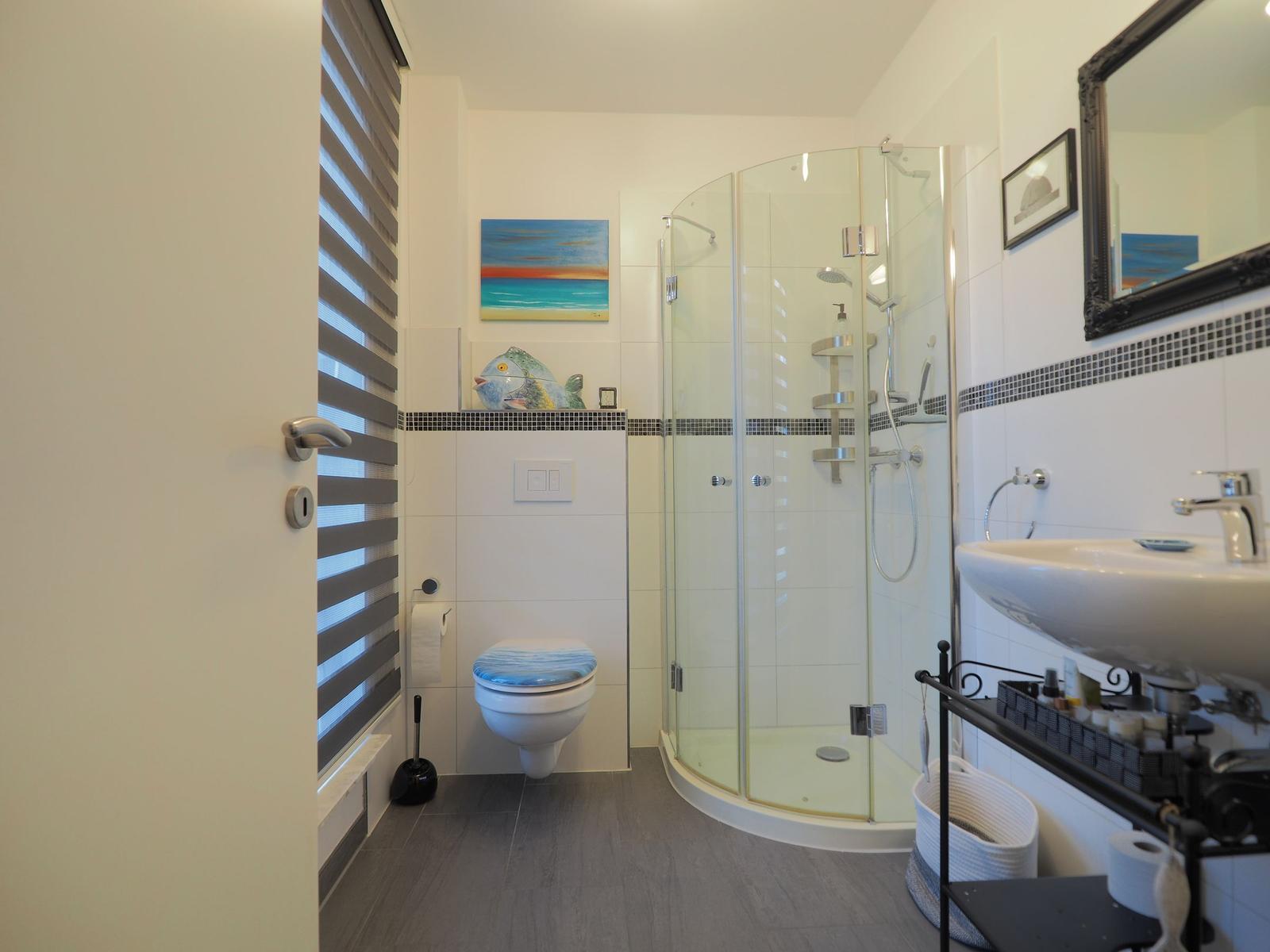 Badezimmer mit Dusche, Waschbecken und Toilette. Wandgestaltung mit Mosaik und Bildern.