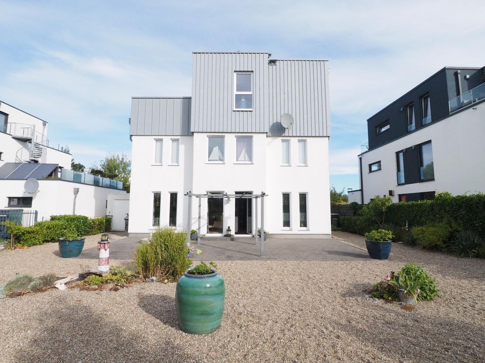 Moderne Villa mit Terrasse und Garten. Große Fenster und graue Dachziegel.