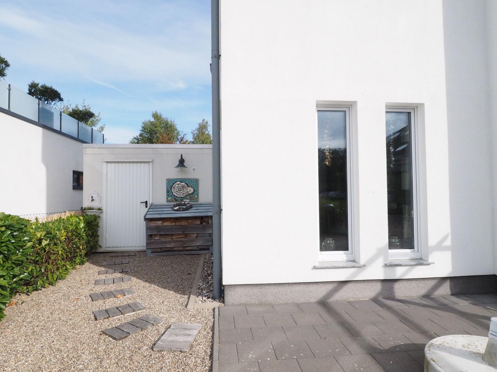 Hinterhof mit Steintreppe, Holzbank und weißen Fenstern an modernem Haus.