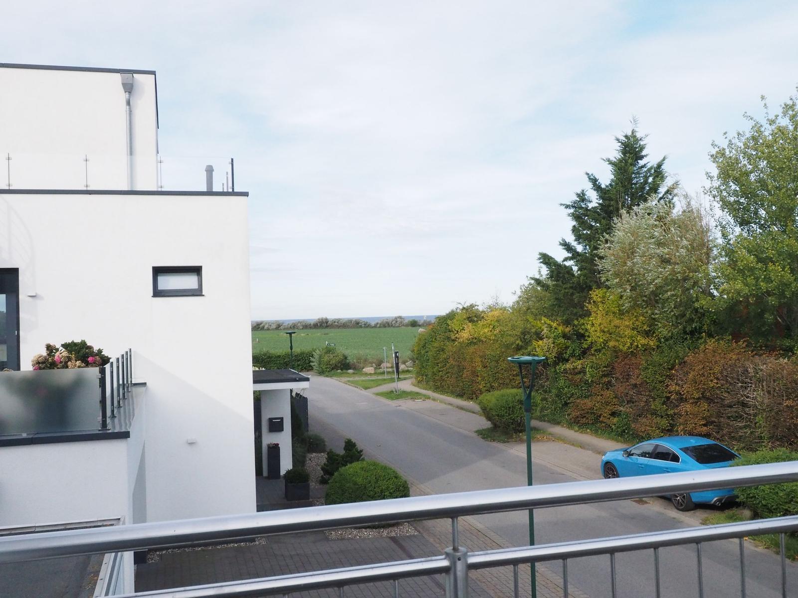 Blick von Balkon auf Straße, Grünflächen und blauen Wagen.