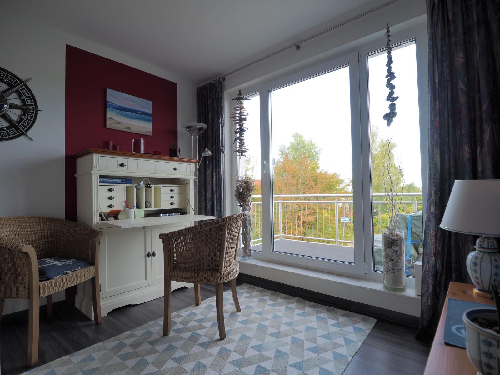 Ein Arbeitszimmer mit Schreibtisch, zwei Stühlen und großem Fenster zum Balkon.