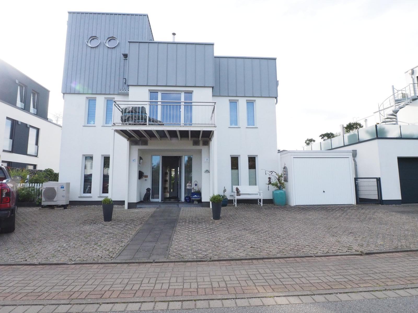 Moderne Villa mit Balkon, Eingang und Garage. Pflanzen und Steinplatten vor dem Haus.