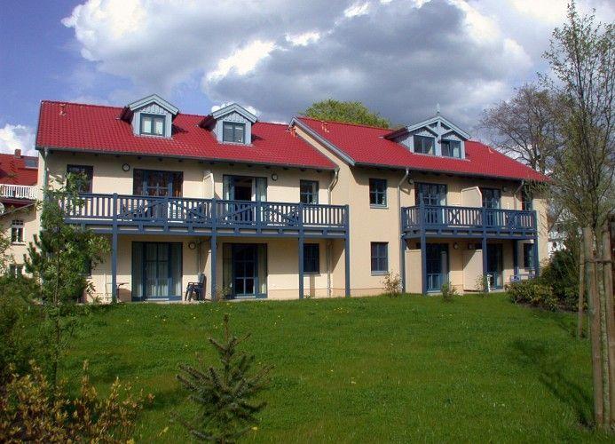 Zweistöckiges Haus mit rotem Dach und blauen Balkonen auf grünem Grundstück.