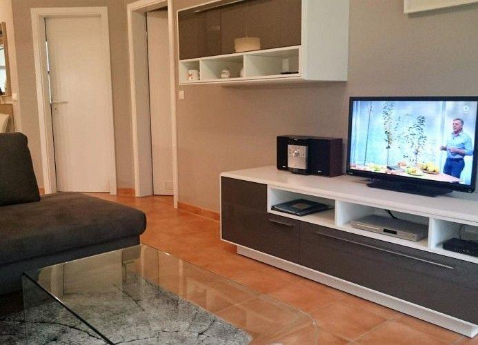 Wohnzimmer mit Sofa, Glas-Tisch und TV auf weißen Schränken.