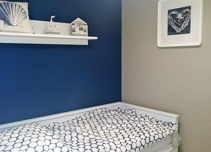 Ein Bett mit gemusterter Bettwäsche, blaue Wand, weiße Regal mit Dekoration und Wandbild.