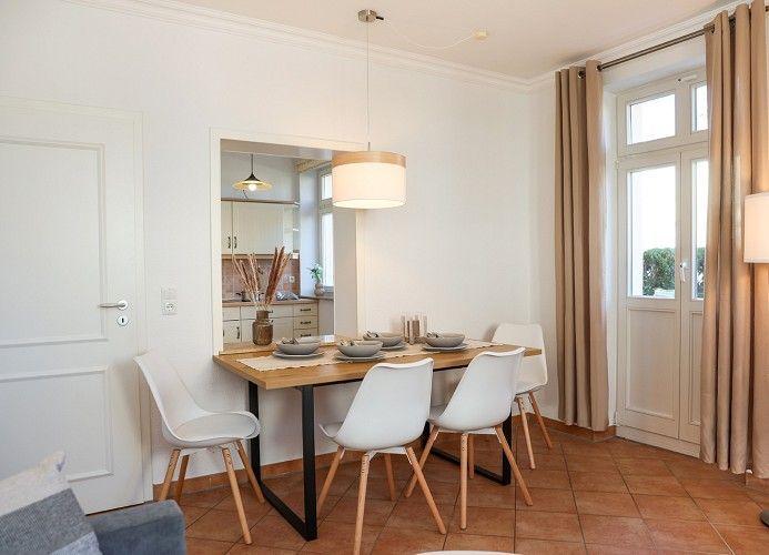 Essbereich mit Holztisch, weißen Stühlen und Fenster mit Vorhängen.