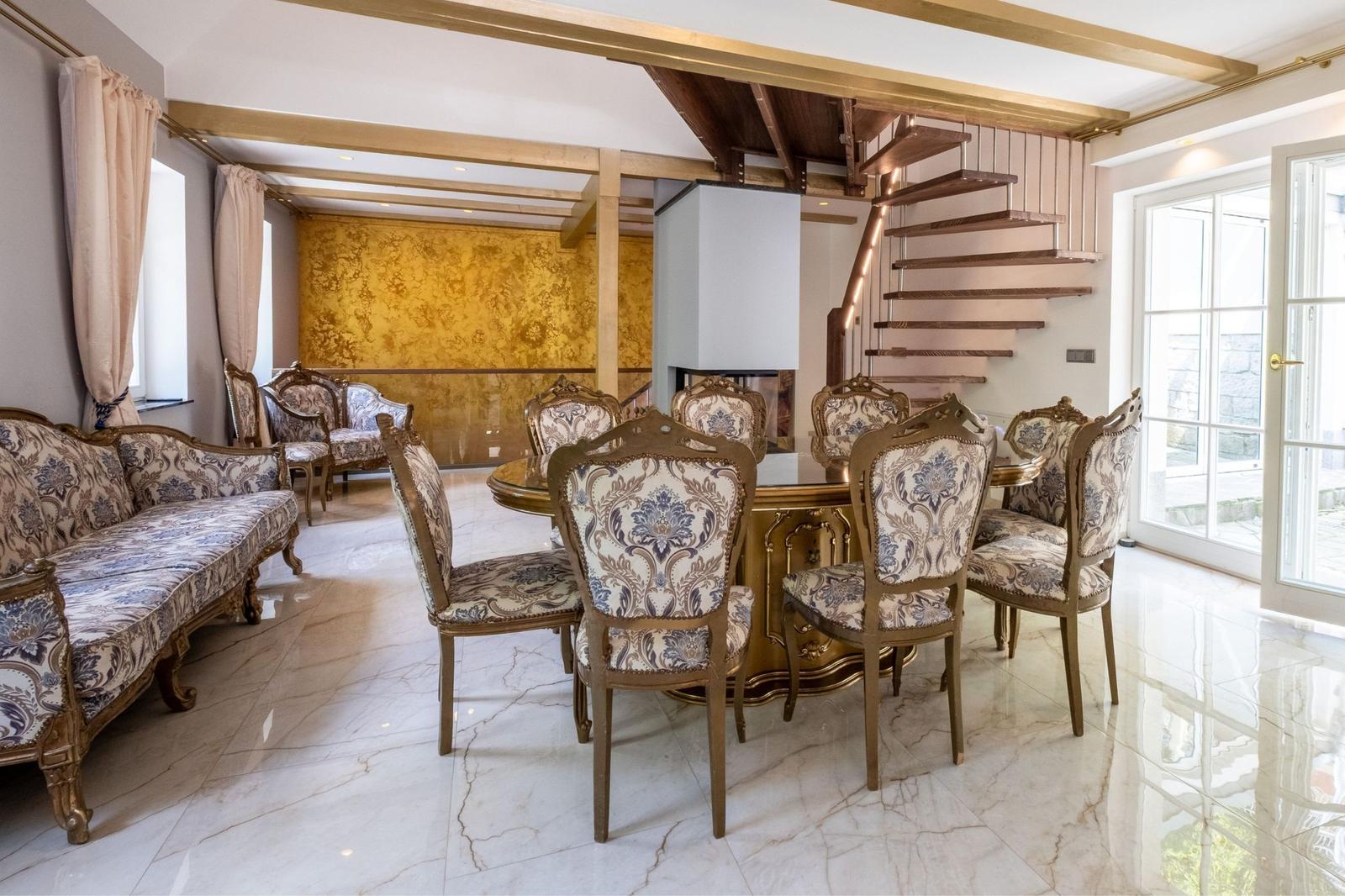 Esszimmer mit goldenem Tisch, Stühlen und Sofa. Hintergrund: goldene Wand und Treppe.