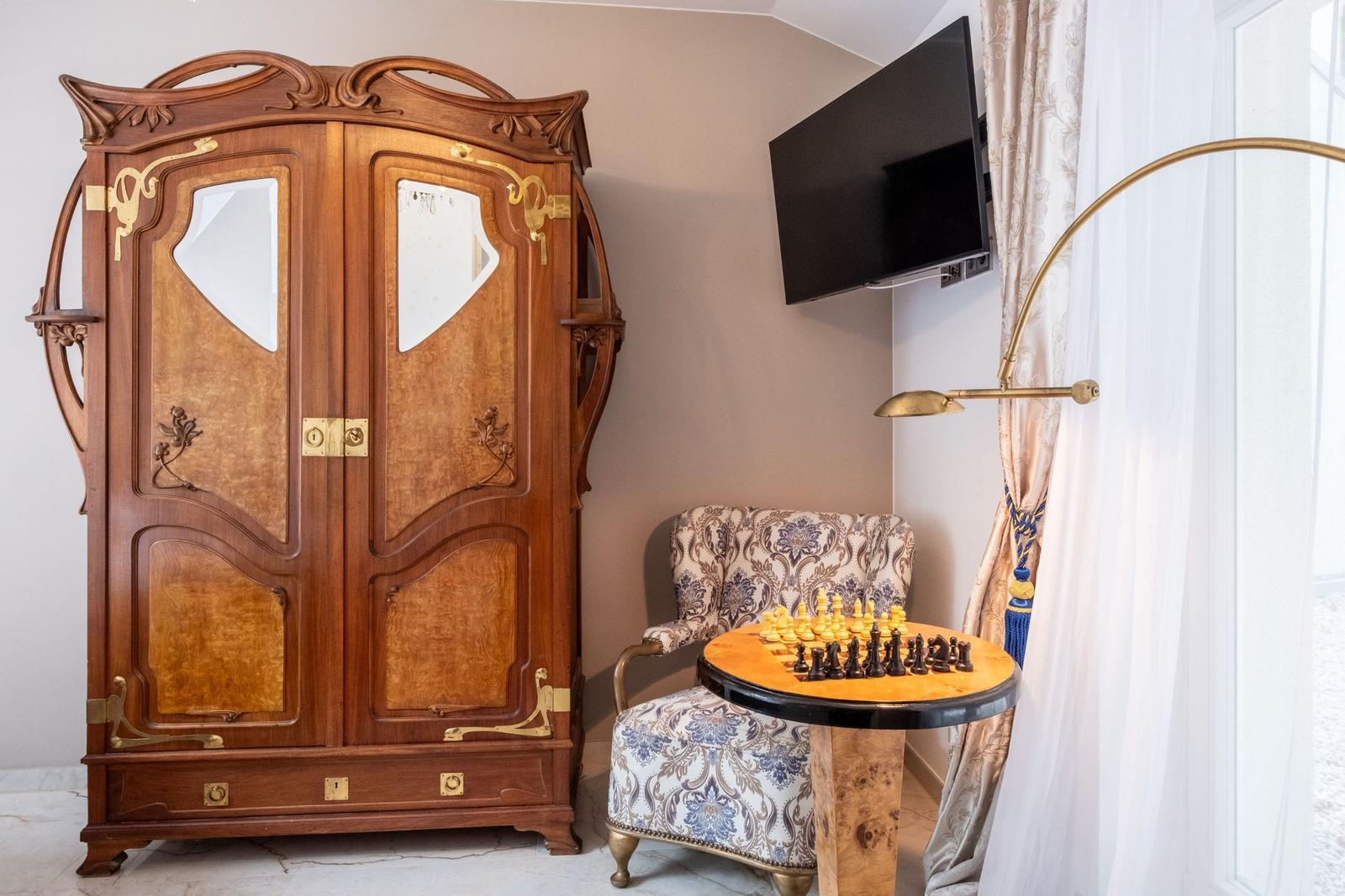 Ein Raum mit einem großen Schrank, einem Sessel und einem Schachbrett auf einem Tisch.