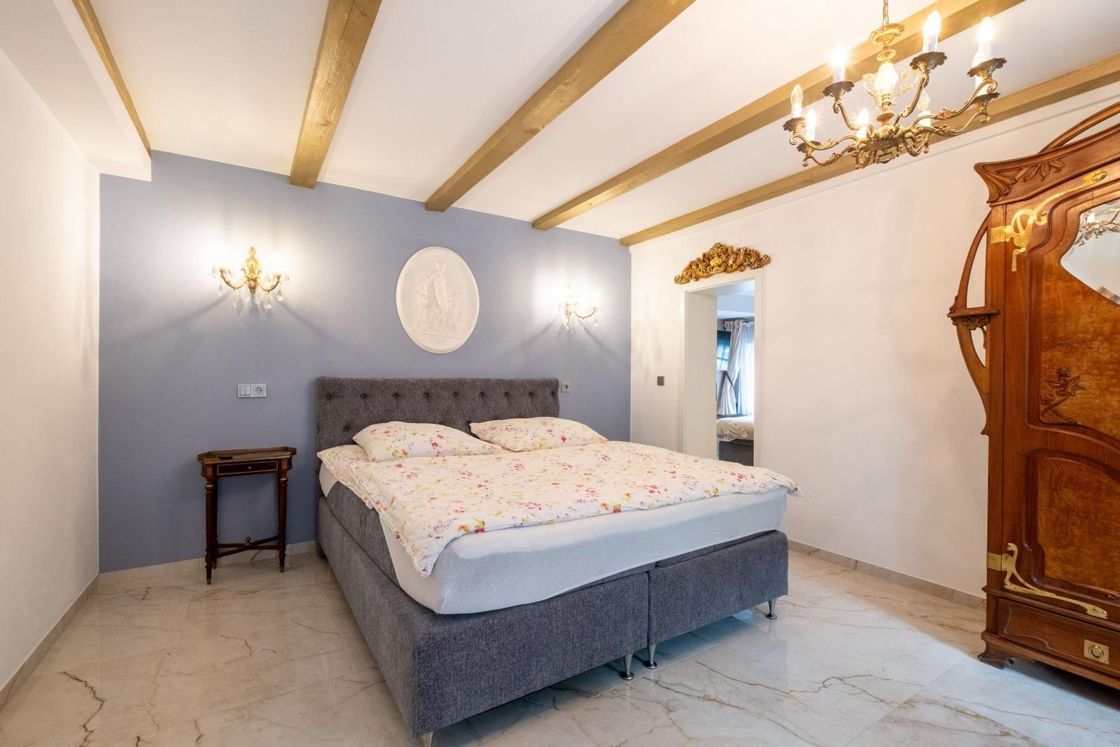 Schlafzimmer mit Bett, Schrank und Kronleuchter. Holzbalken an der Decke.