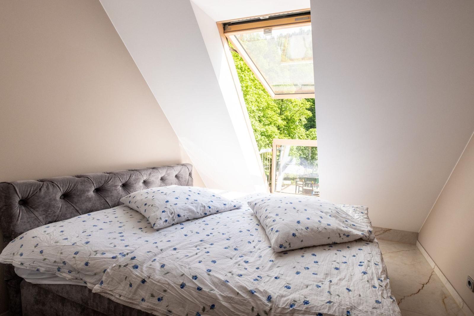 Schlafzimmer mit Dachfenster und Blick auf grüne Bäume.