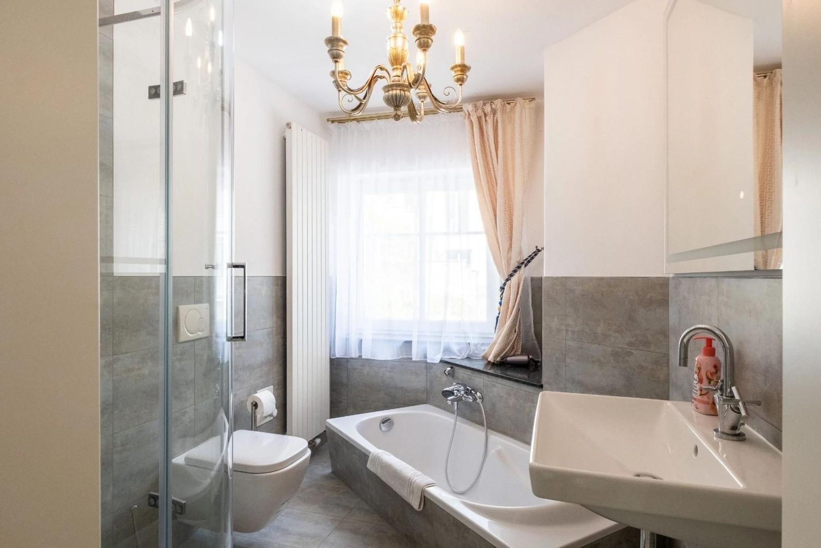 Badezimmer mit Badewanne, Dusche, Waschbecken und Fenster mit Vorhängen.