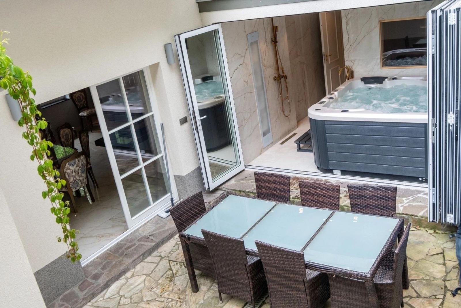 Terrasse mit Sitzgruppe, Whirlpool und Blick in das Badezimmer.