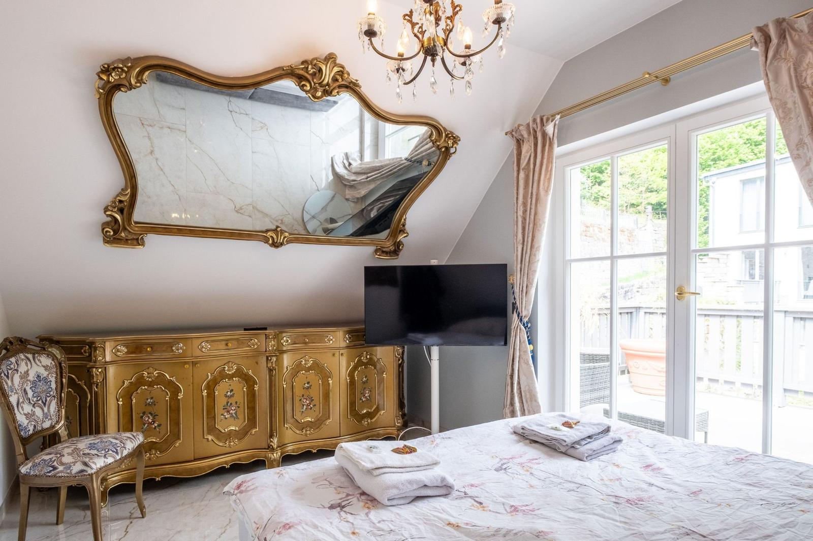 Schlafzimmer mit goldenem Schrank, Spiegel und TV. Fenster mit Blick auf Balkon.