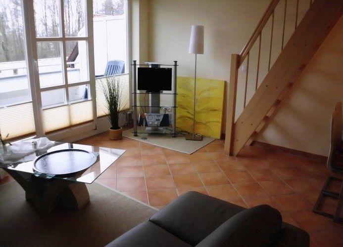Wohnzimmer mit Glas-Tisch, Sofa, Fernseher und Holztreppe