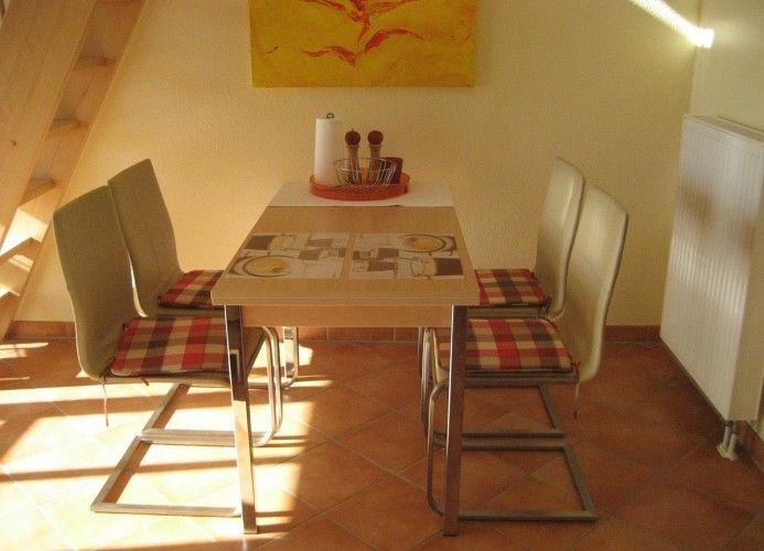 Esszimmer mit Tisch, vier Stühlen und Wandbild. Holztreppe und Heizkörper sind sichtbar.