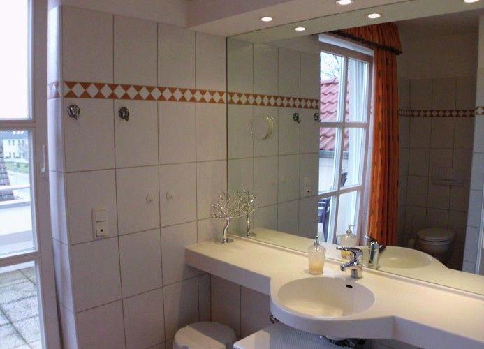 Badezimmer mit Waschbecken, Spiegel und Fenster. Fliesenwand mit dekorativer Bordüre.