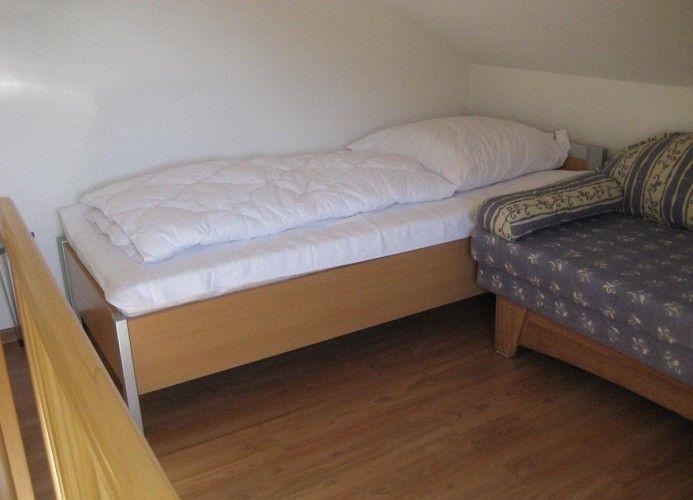 Ein Schlafzimmer mit einem Bett und einem Sofa. Holzfußboden und schräge Decke.