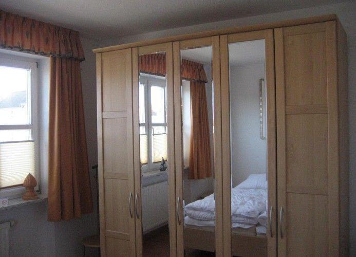 Schlafzimmer mit Spiegelschrank, Fenster und Vorhängen.