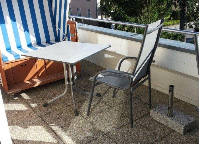 Terrasse mit blau-weißem Liegestuhl, Tisch und Stuhl. Geländer und Pflanzen im Hintergrund.