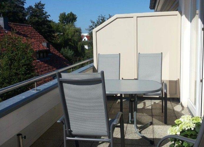 Terrasse mit Tisch und drei Stühlen, Blick auf Dächer und Bäume.