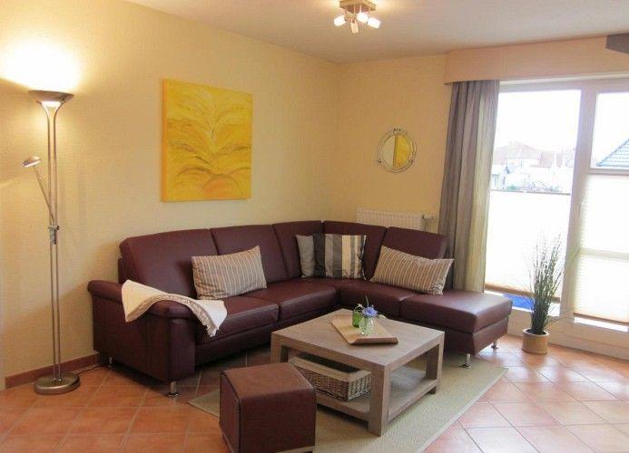 Ein Wohnzimmer mit braunem Sofa, Holztisch und großen Fenstern.