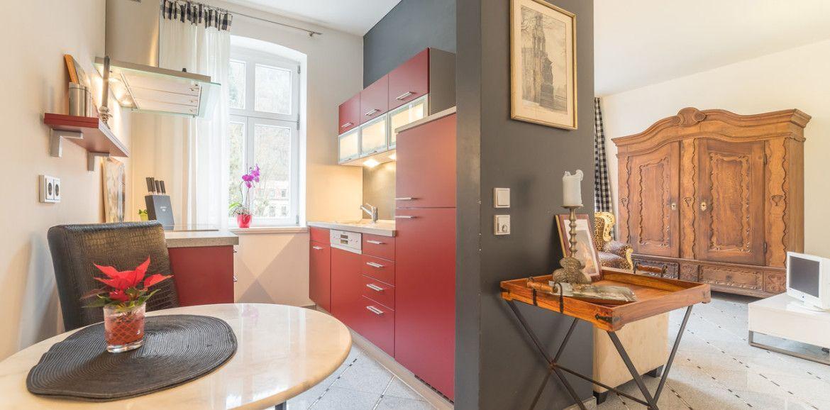 Küche mit roten Schränken und Essbereich. Wohnzimmer mit antikem Schrank und Holztisch.