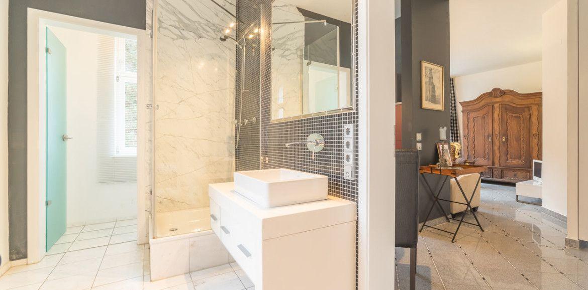 Badezimmer mit Dusche, Waschtisch und angrenzender Schlafzimmer-Ecke.