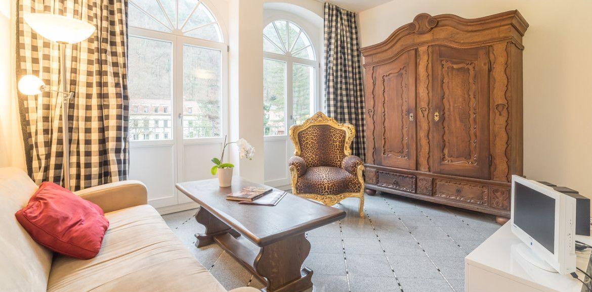 Wohnzimmer mit Sofa, Stuhl, Couchtisch und Schrank. Fenster mit Vorhängen.