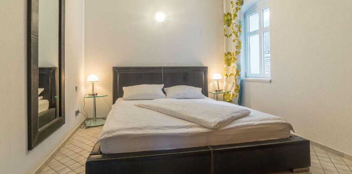 Schlafzimmer mit Doppelbett, zwei Nachttischen und Spiegel an der Wand.