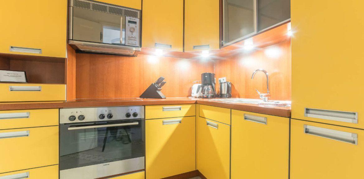 Küche mit gelben Schränken, Edelstahlherd und Mikrowelle.