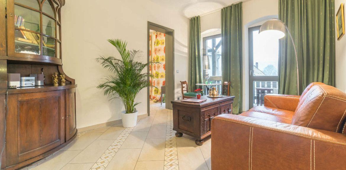 Wohnzimmer mit Ledersofa, Holzmöbel und Pflanze. Durchgang zu einem anderen Raum.