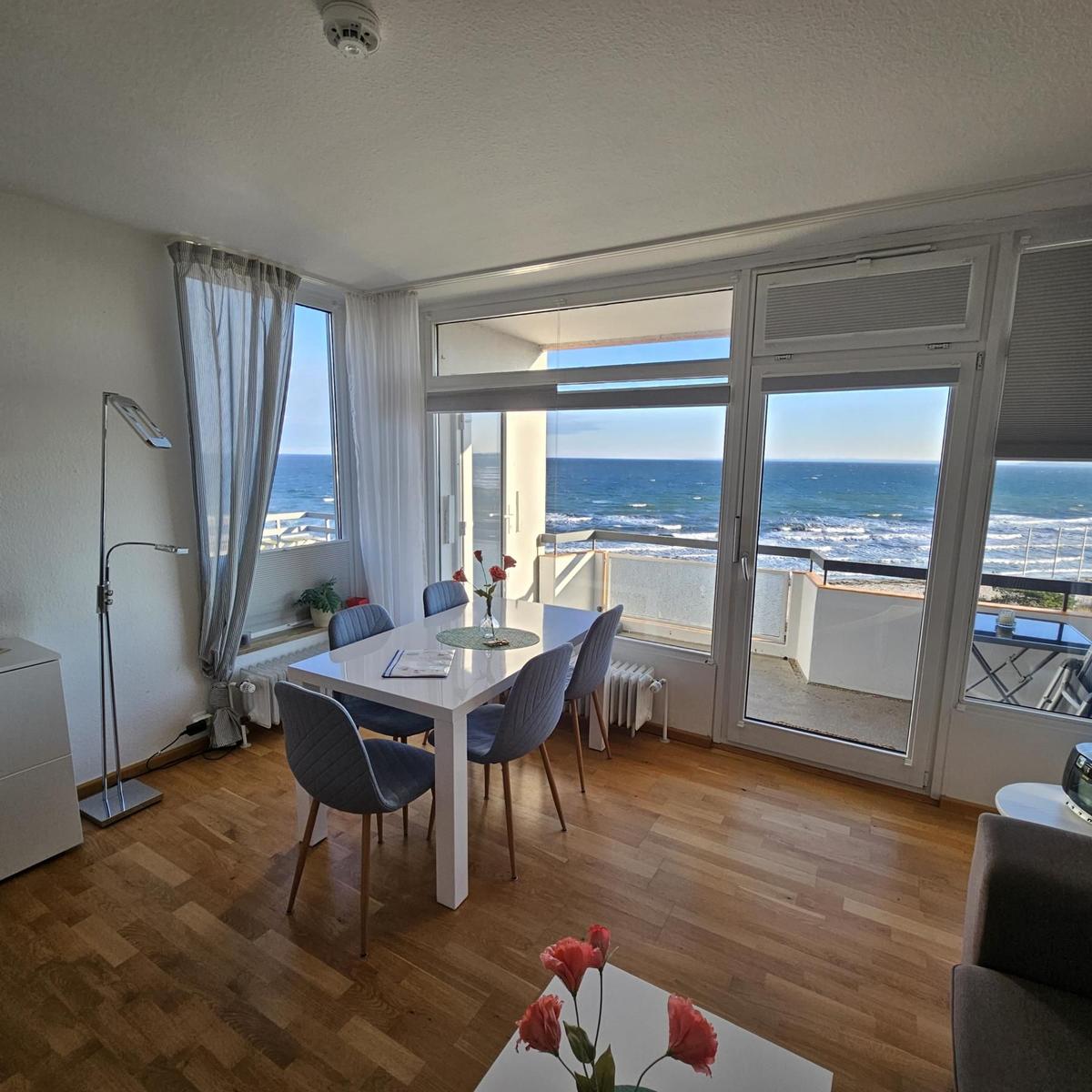 Esszimmer mit Meerblick und Balkon. Holzboden und weiße Möbel.