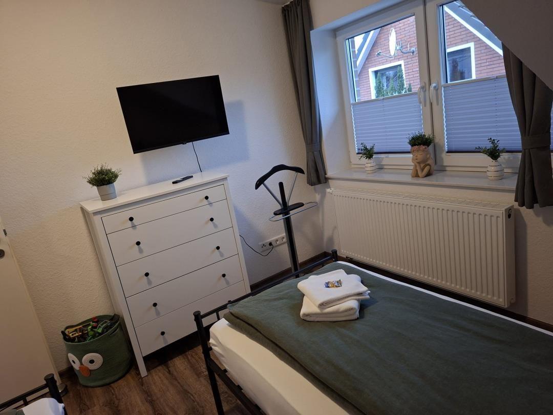 Zimmer mit Bett, Schrank, Fernseher und Fenster mit Blick auf Haus.