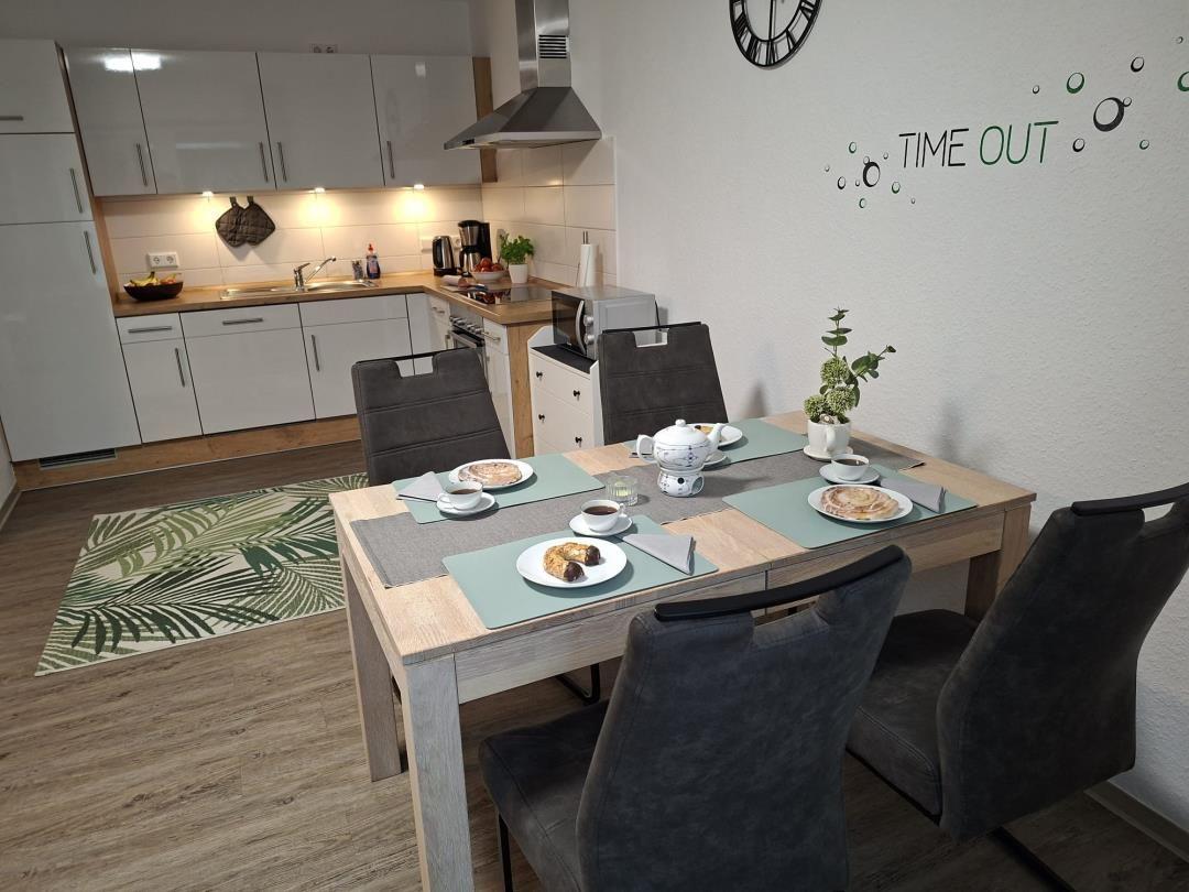 Esstisch mit Stühlen, Küchenbereich und Wanddekoration.