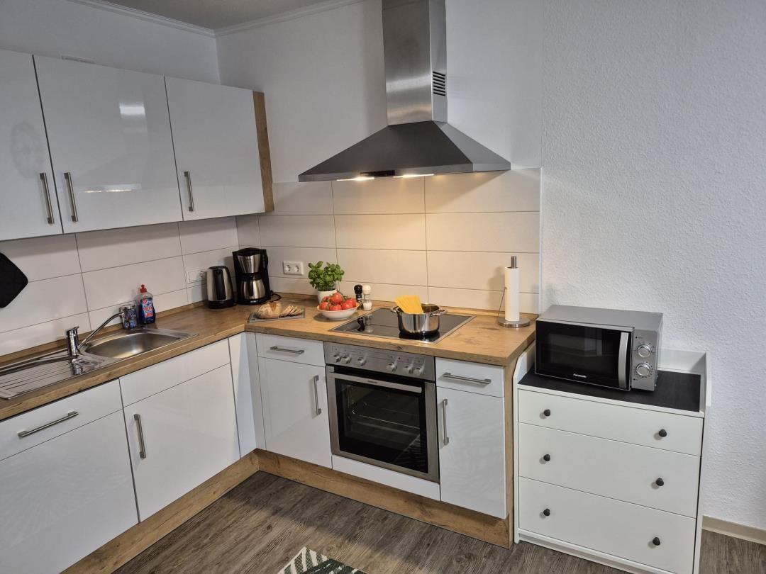 Küche mit weißen Schränken, Edelstahlherd und Mikrowelle.