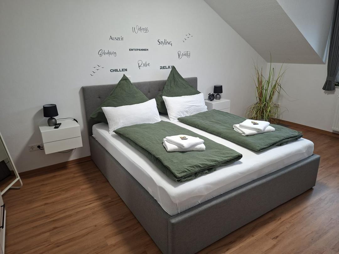 Schlafzimmer mit Doppelbett, grünen Kissen und Wanddekoration.