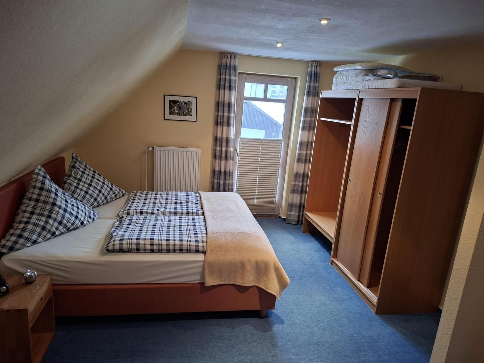 Schlafzimmer mit Dachschräge, Bett, Kleiderschrank und Fenster.