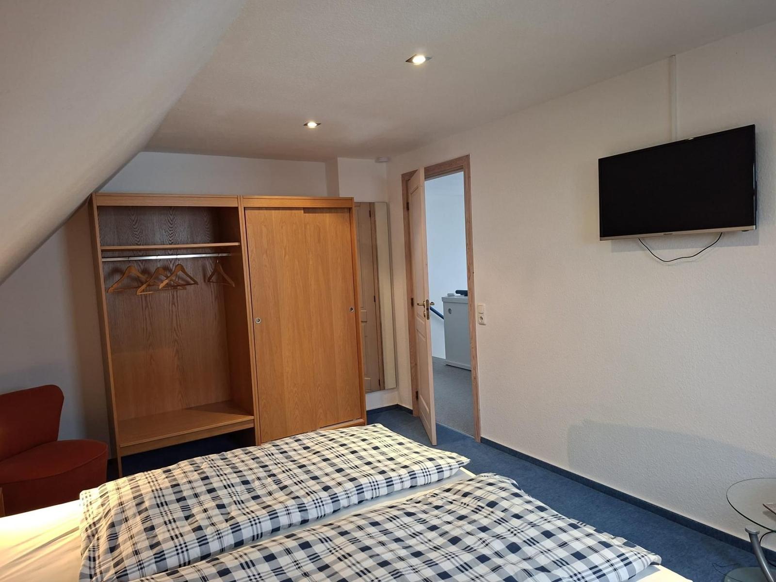 Schlafzimmer mit Bett, Kleiderschrank und Wandfernseher.