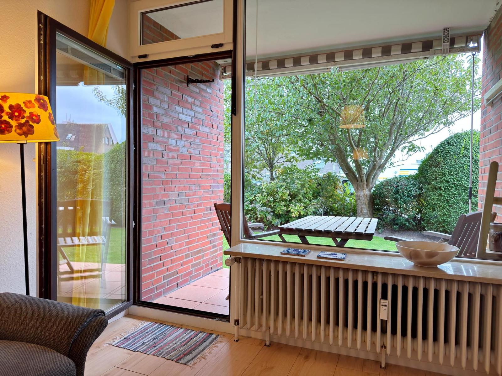 Durchgehendes Fenster mit Blick auf Terrasse und Garten mit Tisch und Stühlen.