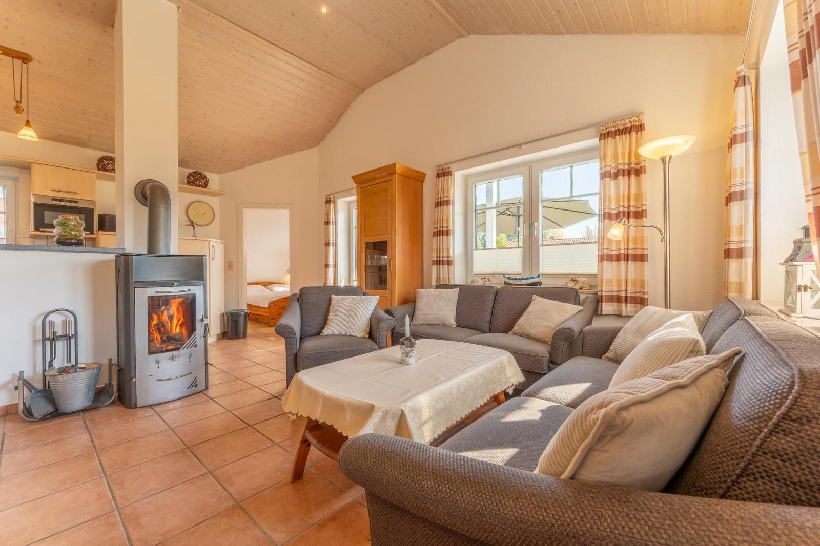 Wohnbereich mit Kaminofen, Sofa und Tisch. Küche und Schlafzimmer sind sichtbar.