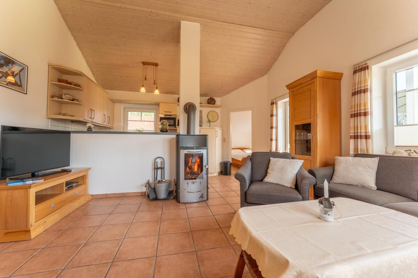 Wohnzimmer mit Kamin, Sofa, TV und Küche im Hintergrund.