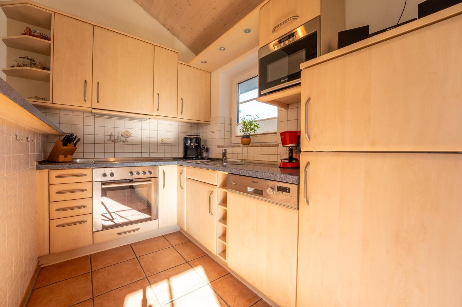 Küche mit Holzschränken, Edelstahlgeräten und Fenster.