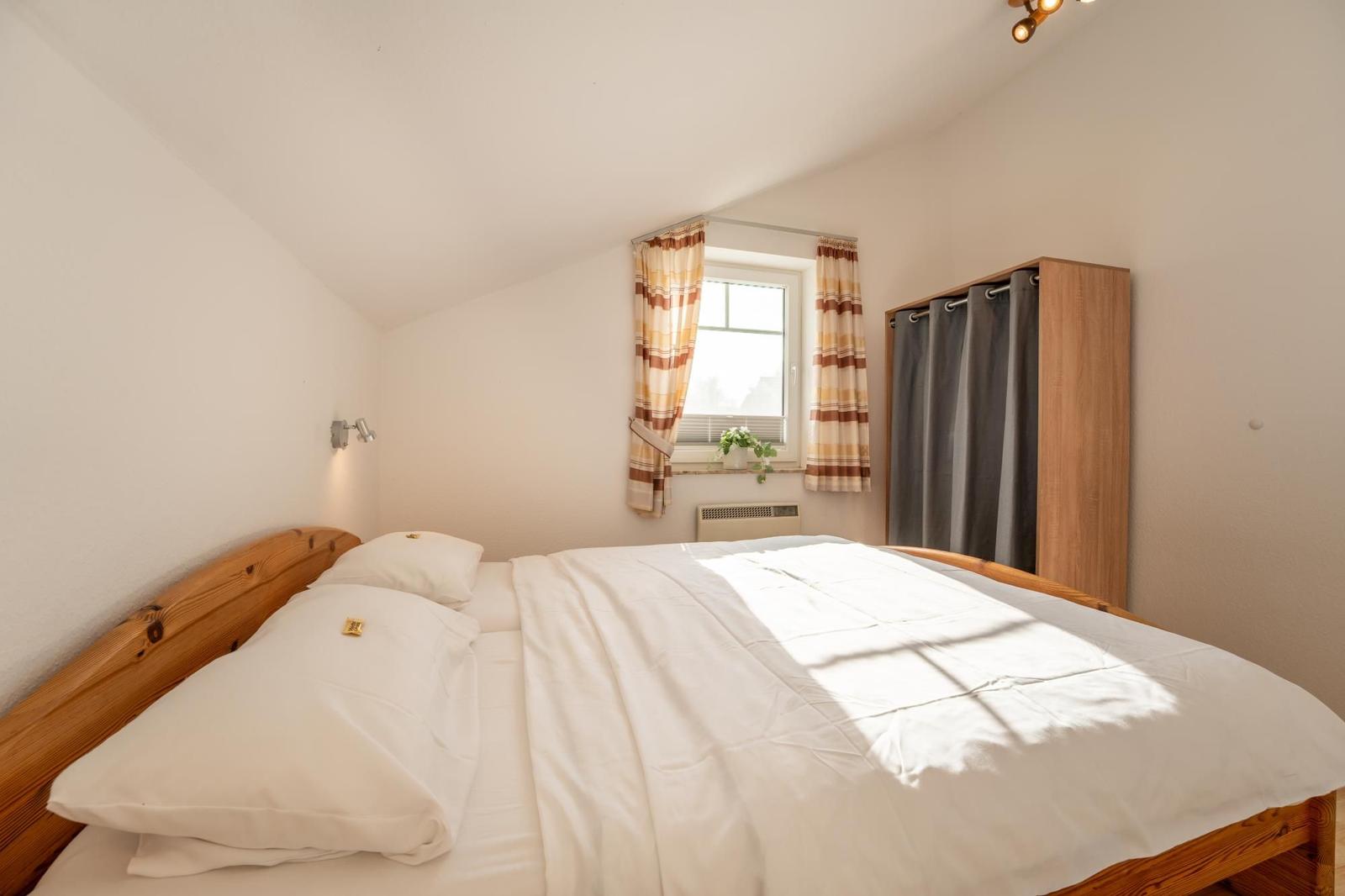 Ein Schlafzimmer mit Holzbett, Fenster mit Vorhängen und Kleiderschrank.