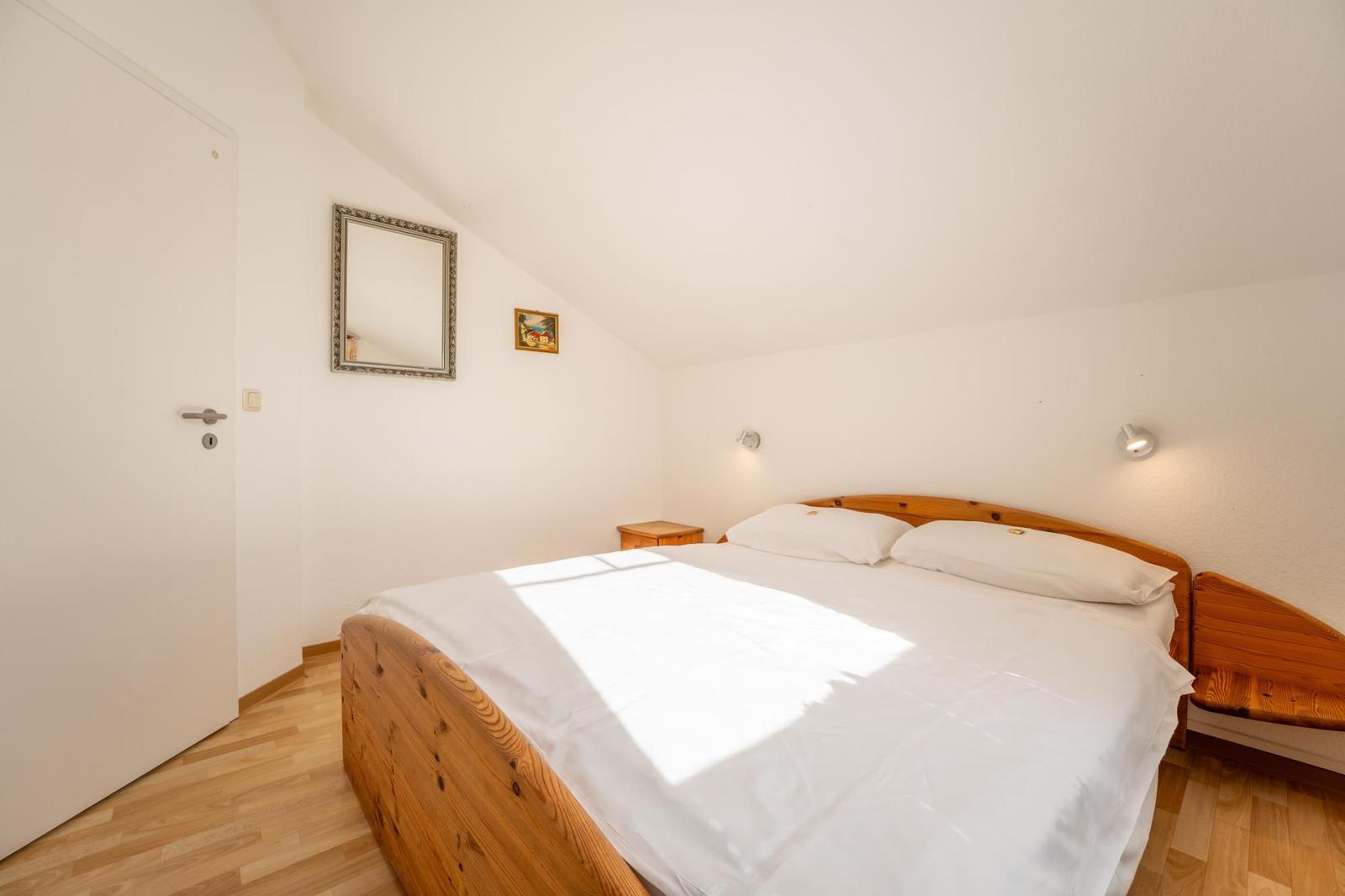 Schlafzimmer mit Holzbett, Spiegel und Nachttisch unter schrägem Dach.