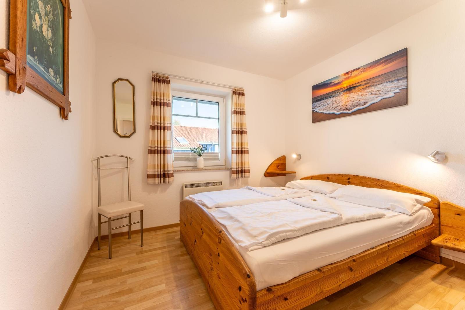 Ein Schlafzimmer mit Holzbett, Fenster, Vorhängen und Wandbildern.