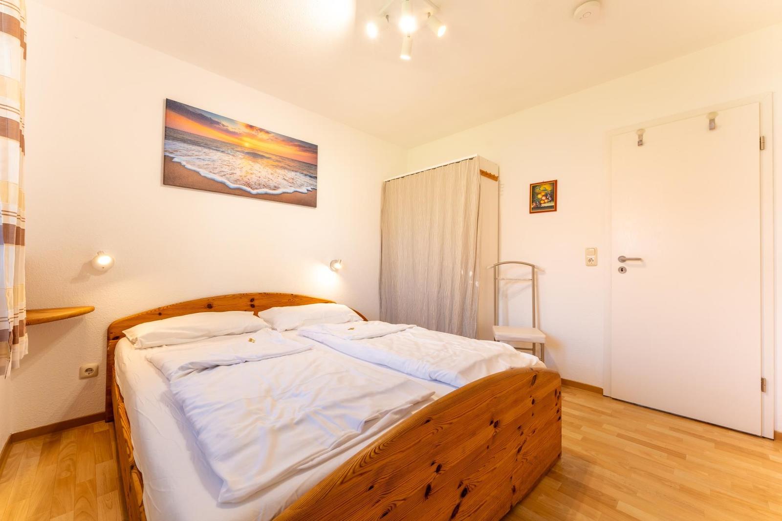 Schlafzimmer mit Doppelbett, Holzboden und Wandbild von Sonnenuntergang.