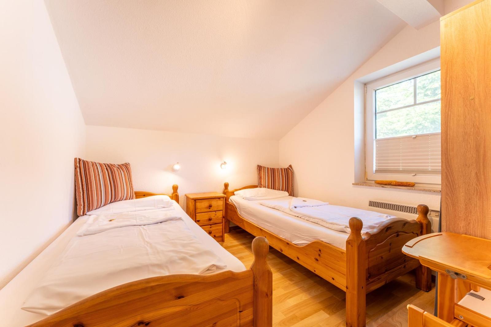 Zwei Einzelbetten mit Holzgestell, Nachttisch und Fenster mit Jalousie.