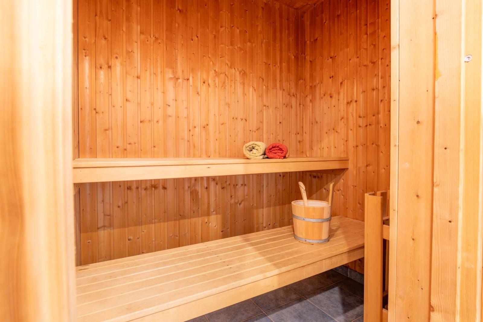 Sauna mit Holzwand, Bank und Eimer mit Löffeln.