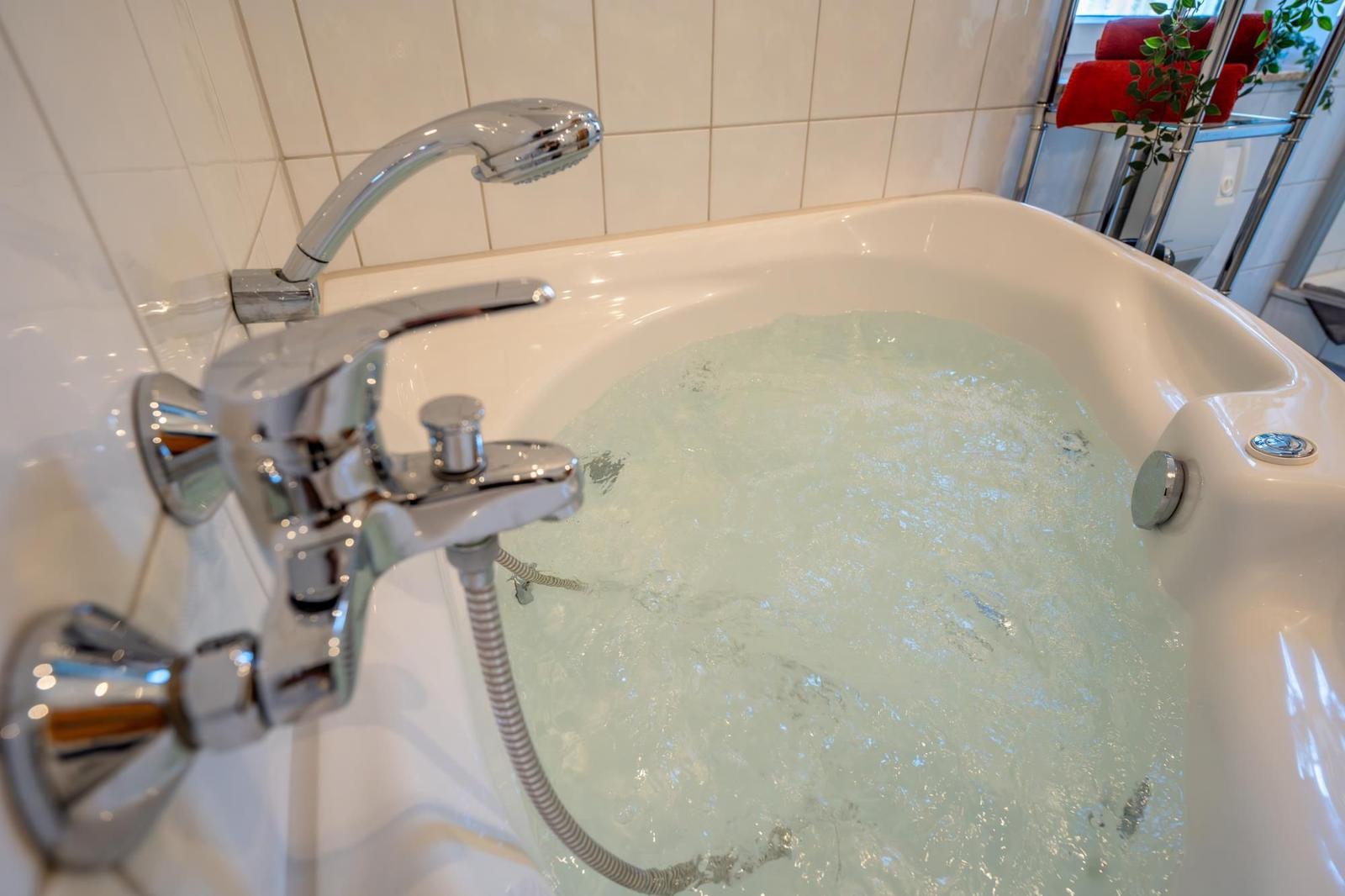 Eine Whirlpool-Badewanne mit Duschkopf und Chromarmaturen in einem hellen Badezimmer.